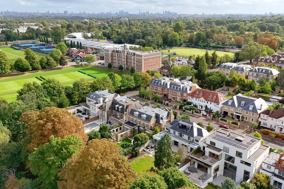 Aerial view over a street of detached houses and tennis courts, with a city skyline on the horizon