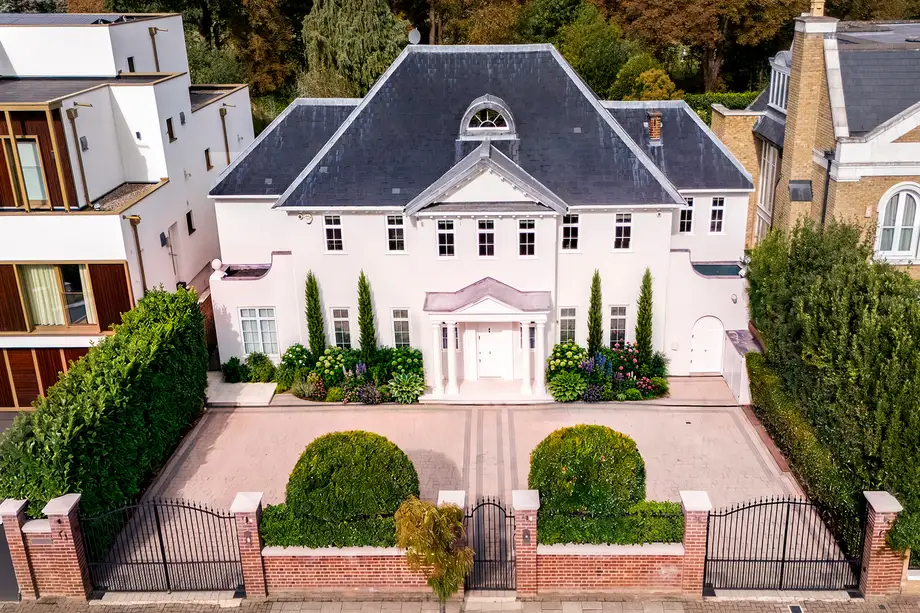 Aerial front elevation of a white villa behind a walled and gated forecourt